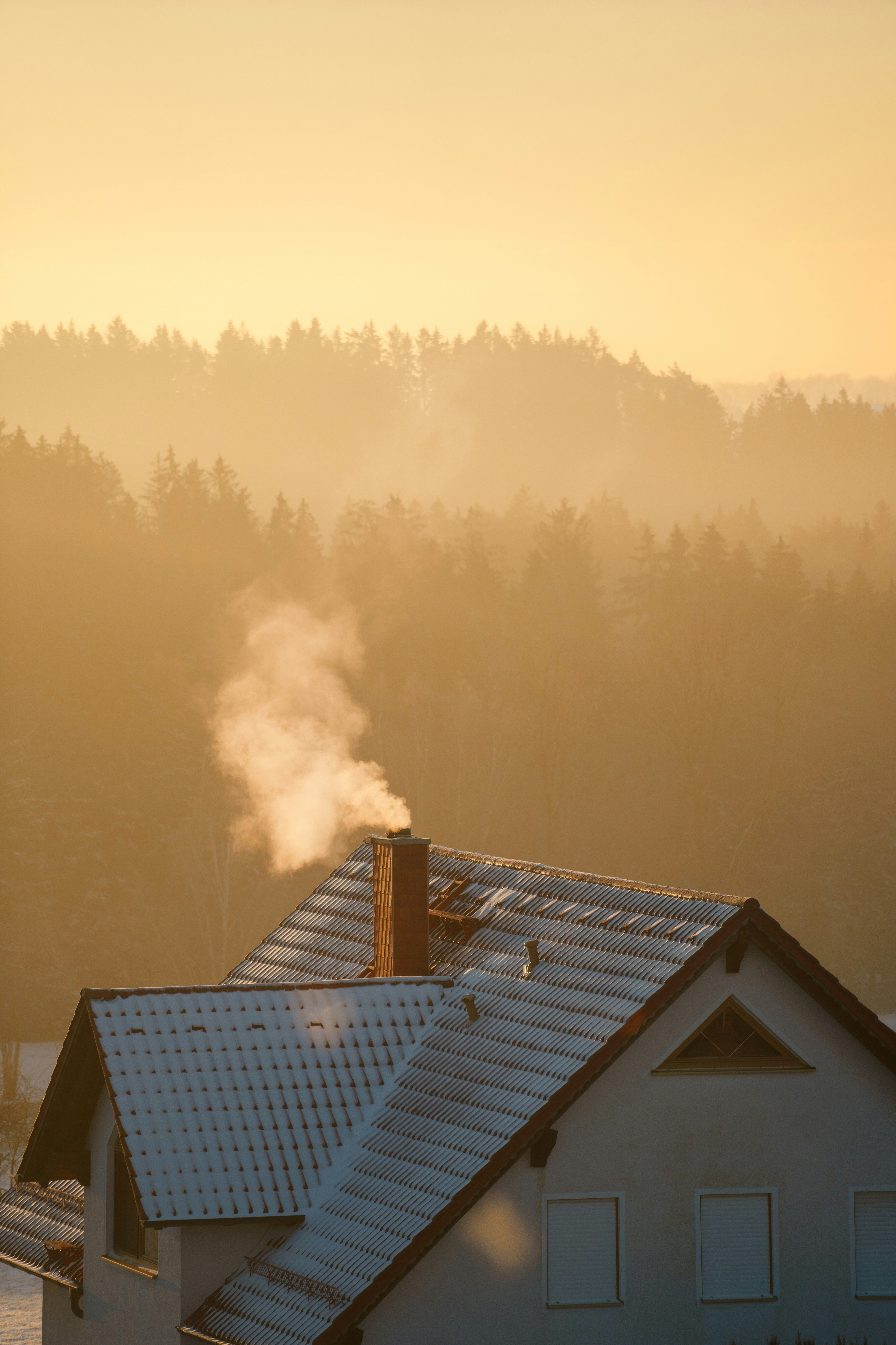 Ein Dach von einem Haus bei Abendsonne mit einem Schornstein aus dem es dampft