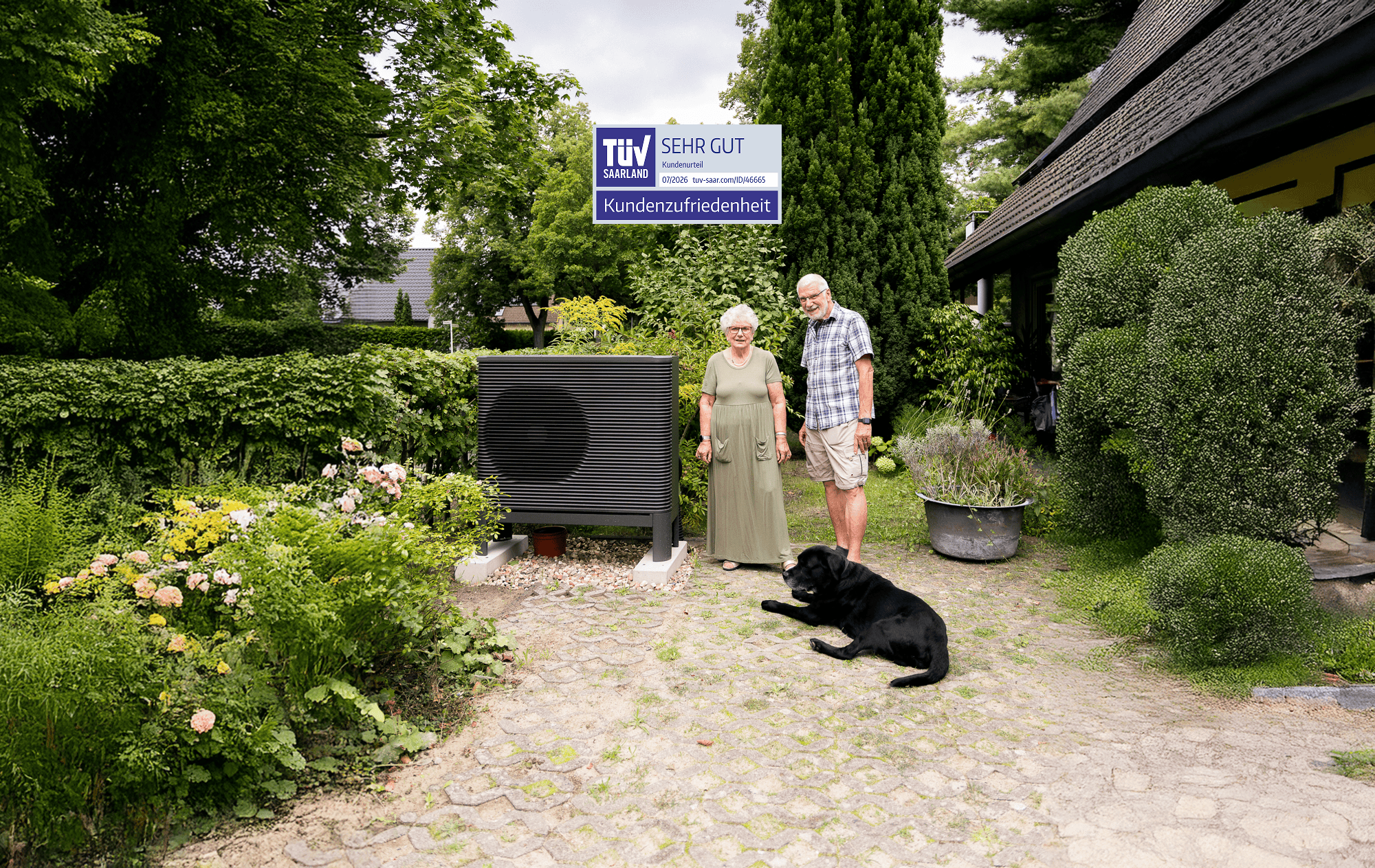 Ein Mann und eine Frau stehen mit ihrem Hund neben einer Aira Wärmepumpe. Über der Wärmepumpe ist das TÜV-Saarland-Siegel zu sehen.