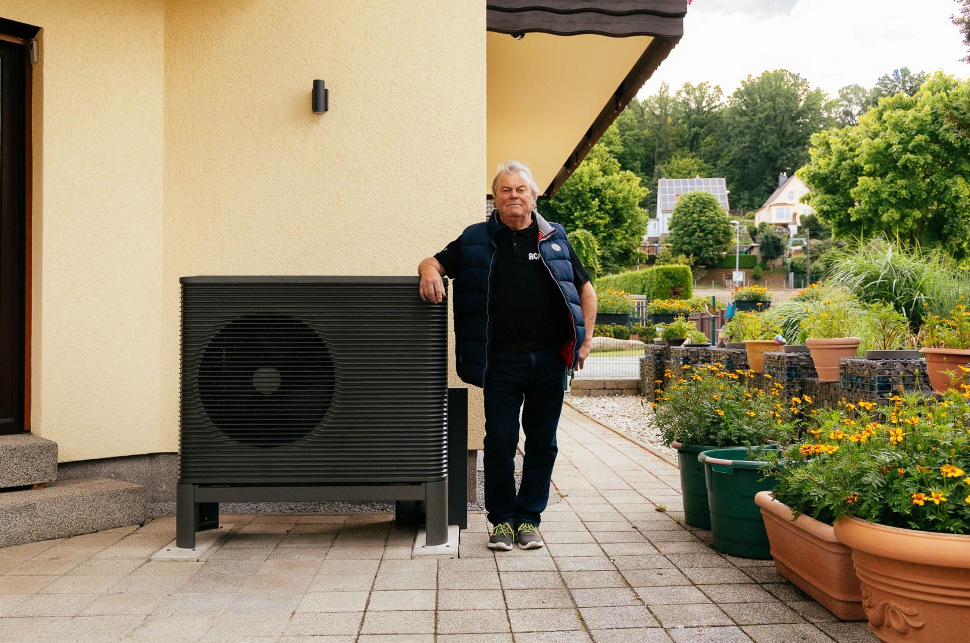 Kunde eines Einfamilienhauses steht vor einer gelben Hauswand neben seiner Wärmepumpe