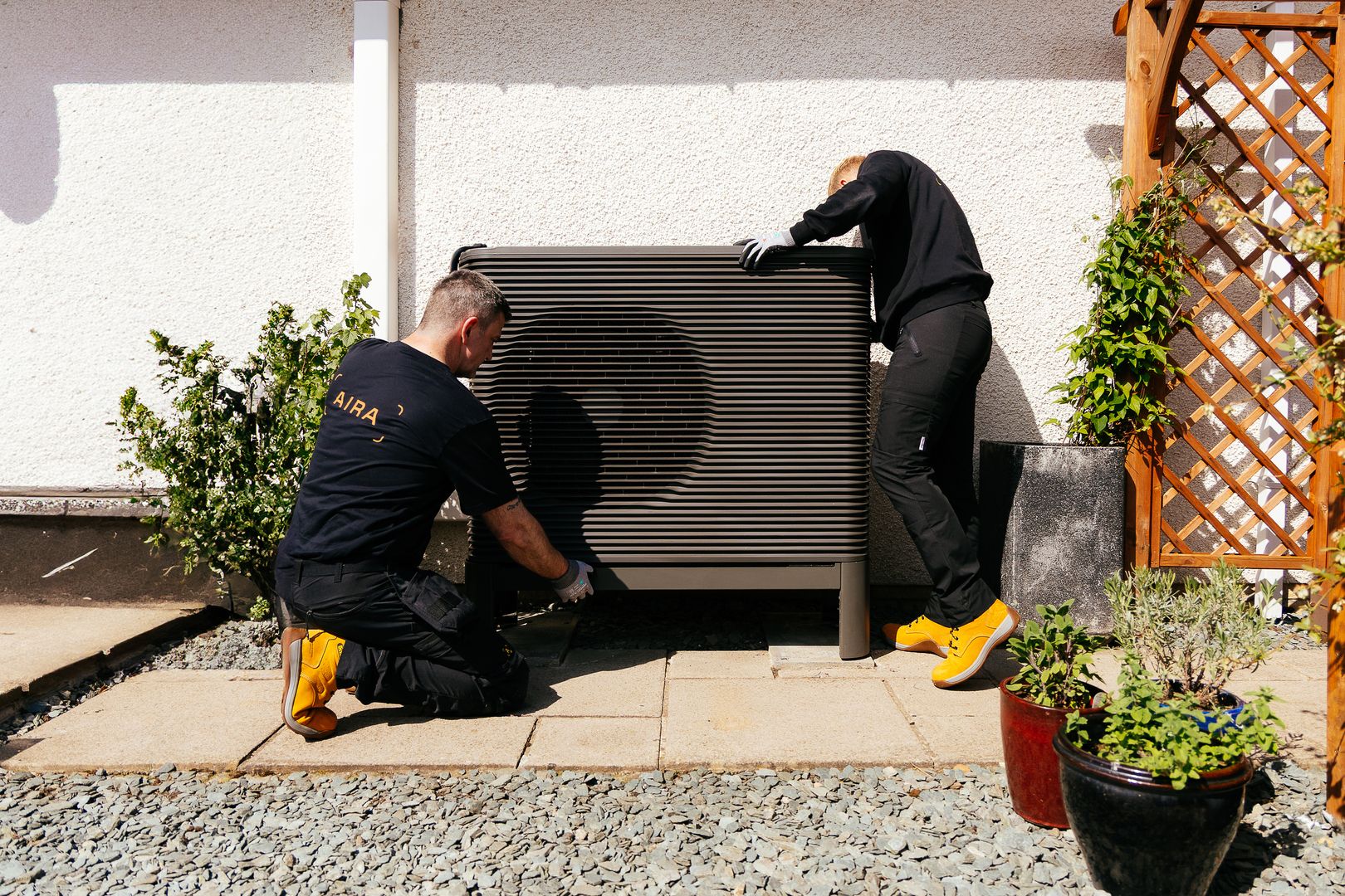Zwei Installateure installieren eine Wärmepumpe vor einer weißen Hauswand