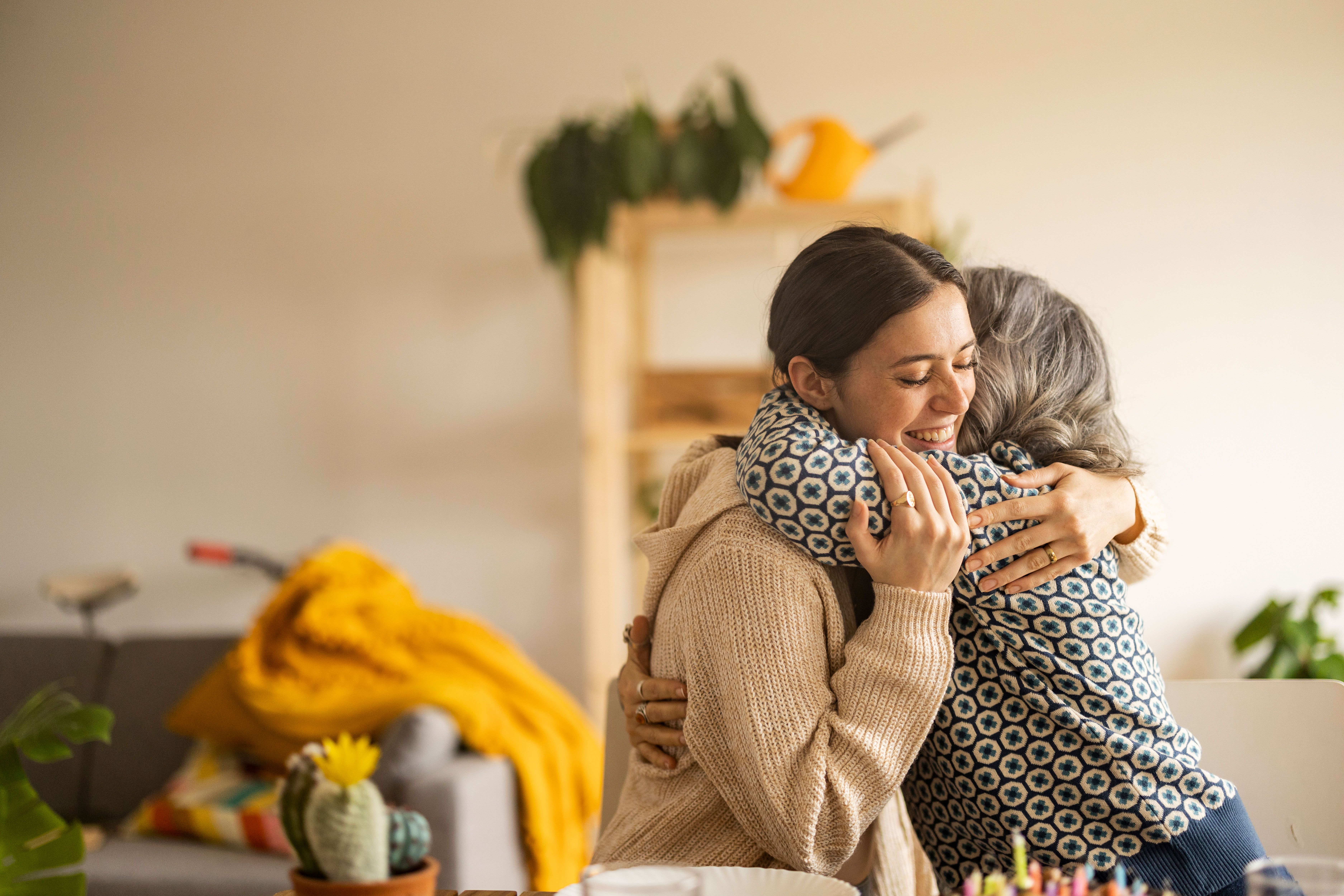 Tochter und Mutter umarmen sich in ihrem warmen Zuhause und strahlen