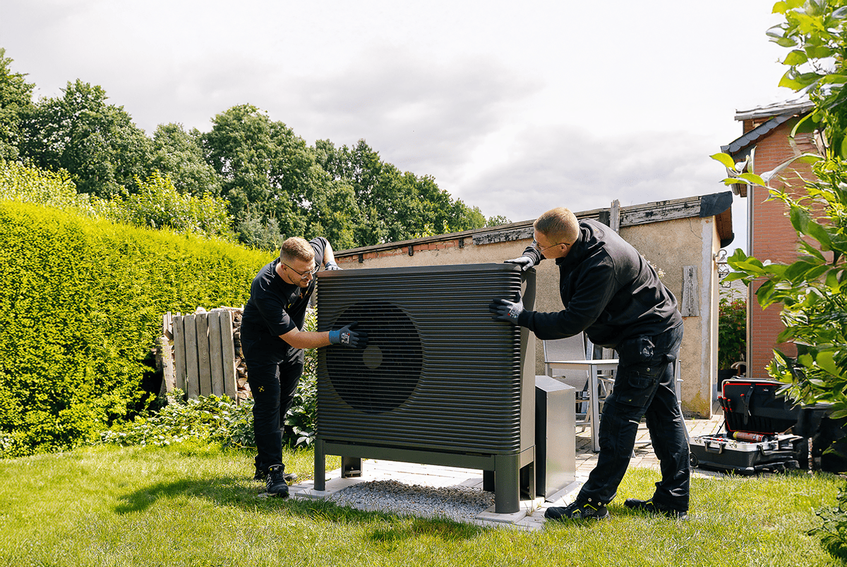 Zwei Installateure installieren eine Wärmepumpe im Garten